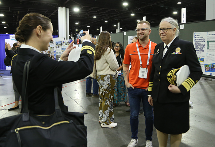 A staff woman for HHS's Rachel Levine takes a photo of Levine with a young white man who was showing Levine his poster during the APHA poster session. 